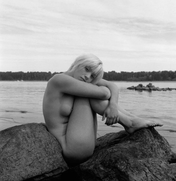 A nude woman curled seated on 2 rocks